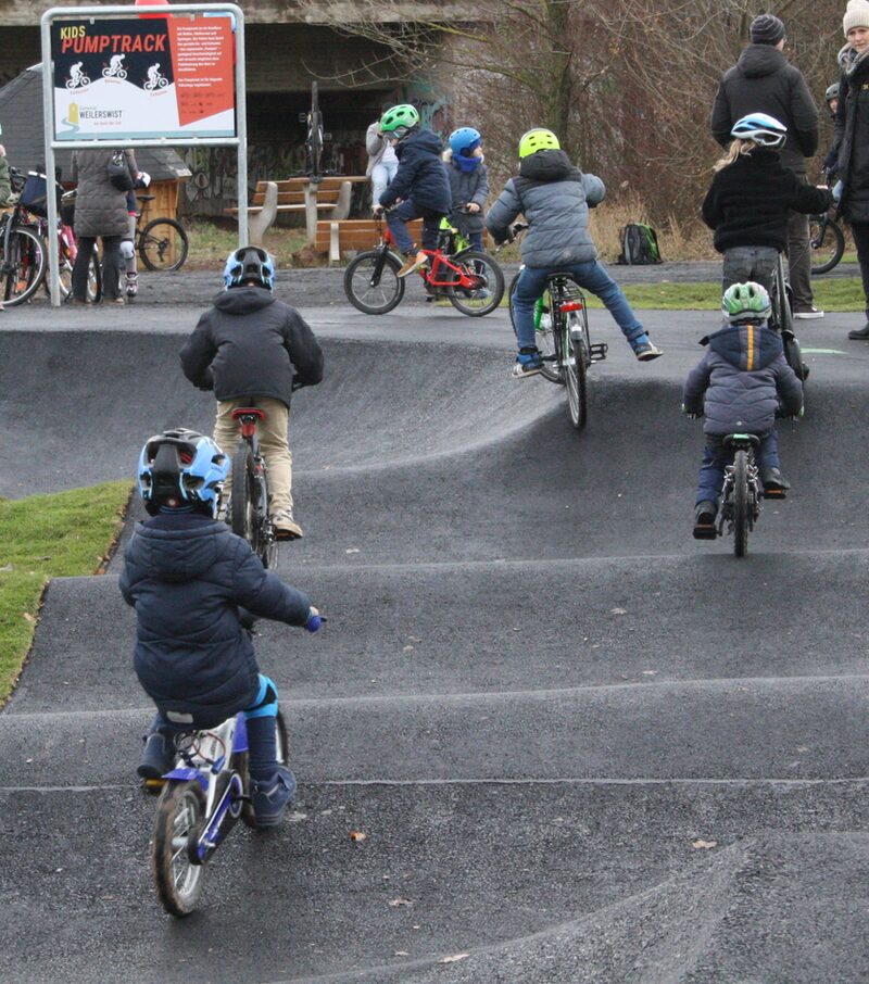 Zu sehen ist ein Ausschnitt des Kidspumptracks. Dort fahren viele jüngere Kinder mit ihren Fahrrädern.